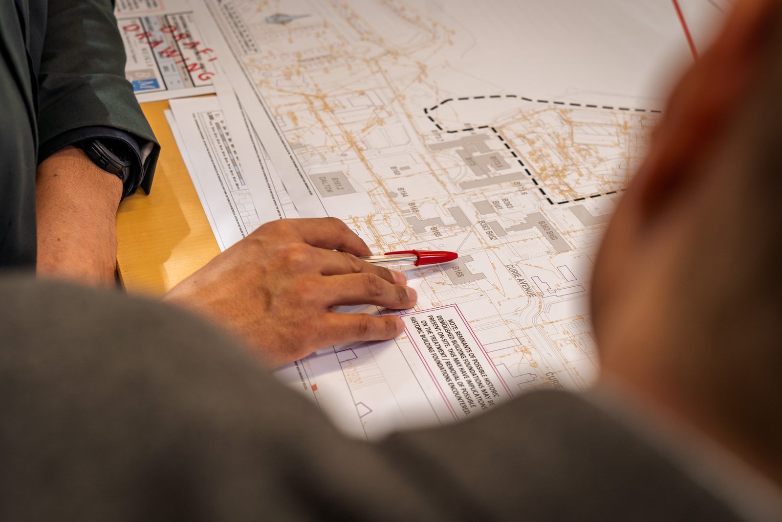 A close up shot of a hand holding a pen over some structural plans laid on a table