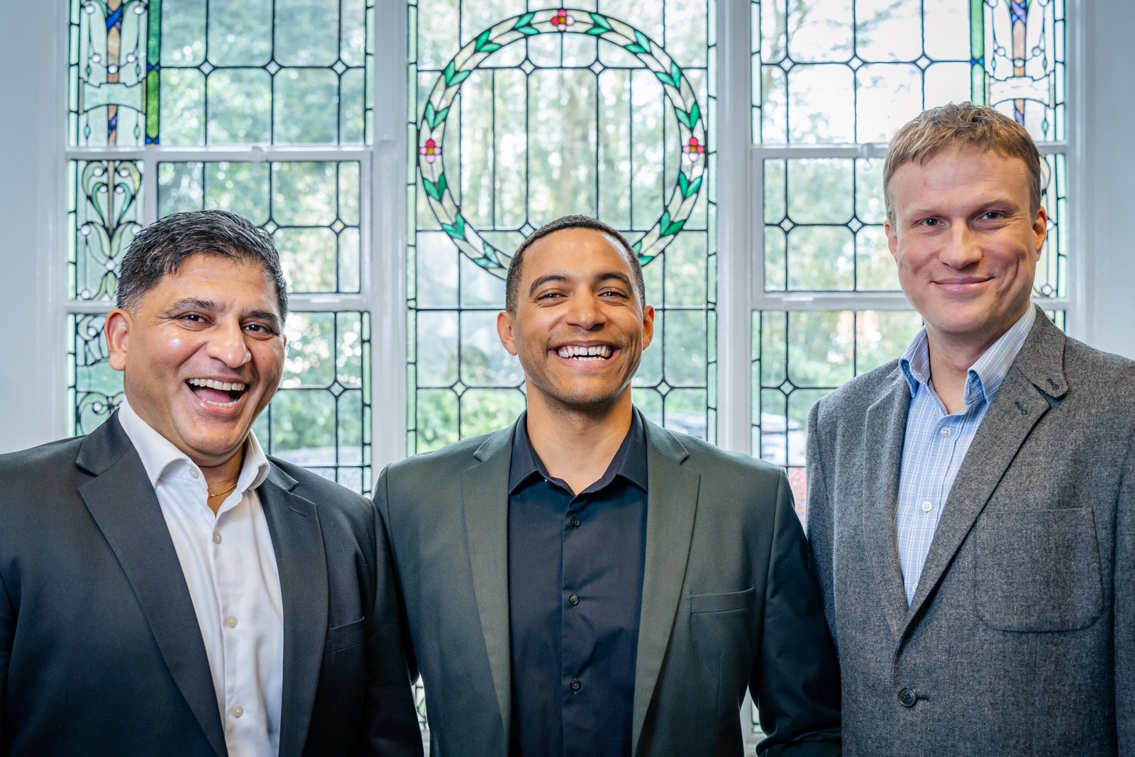 3 men standing in front of a stained glass window in suits