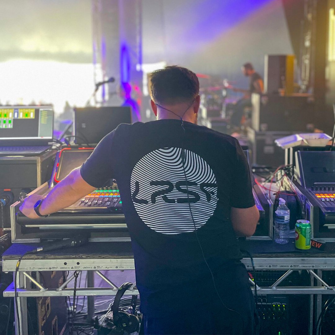 A sound engineer behind a mixing desk wearing a black t-shirt with the letter LRSF printed on the back