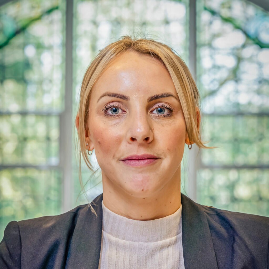 A headshot of a blonde business woman with blonde hair tied behind her head